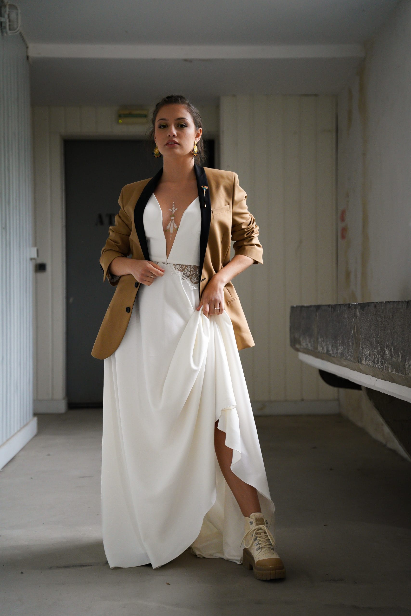 Mariée vêtue d'une robe simple avec un grand décolleté à l'avant, portant élégamment la veste de costume de son marié pour une touche originale